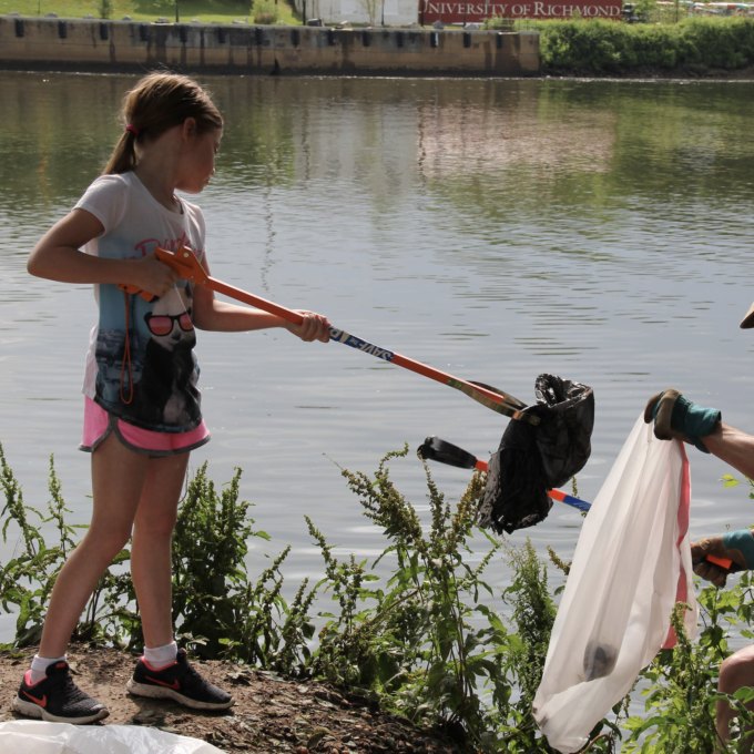 A child picking up trash next to a body of water